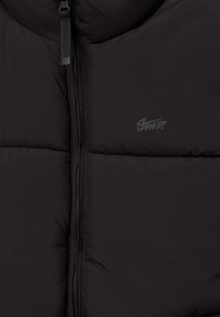 Gilet imbottito nero realizzato in materiale sintetico, con zip frontale, colletto alto e un logo subtile sul petto. Texture liscia.