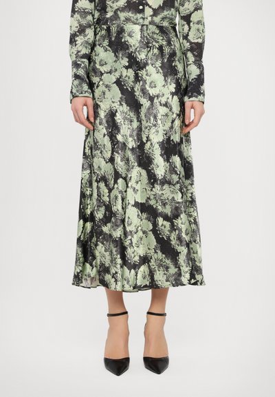 Jupe mi-longue à motif floral noir et vert clair avec une texture fluide, assortie à des escarpins noirs à talons pointus et des sangles de cheville.