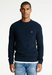 Marineblauer Pullover mit strukturierter Strickware, geripptem Rundhalsausschnitt und Bündchen, ausgestattet mit einem kleinen Logo-Patch auf der Brust.