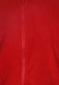 Giacca in pile rossa con zip a tutta lunghezza. Il tessuto è morbido e testurizzato, con una zip liscia e senza ulteriori decorazioni.