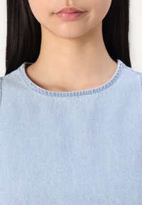 Svijetloplavi denim gornji dio s okruglim izrezom i vidljivim detaljima šivanja. Glatka tekstura, strukturiran oblik, osmišljen za ležernu nošnju.