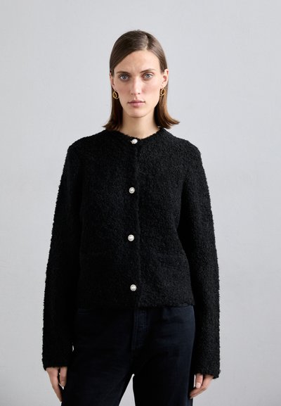 Schwarze strukturierte Jacke mit langen Ärmeln, die fünf dekorative Knöpfe und einen runden Halsausschnitt aufweist. Der strukturierte Stoff verleiht ein gemütliches Erscheinungsbild.