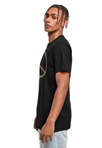 Sort bomulds T-shirt med et farverigt fredssymbol illustreret på forsiden. Kortærmet og med en afslappet pasform, båret med lyseblå jeans.