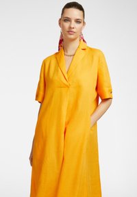 Abito tunica in lino giallo con maniche corte, colletto a punta e tasche laterali. Presenta una texture liscia e una vestibilità rilassata.