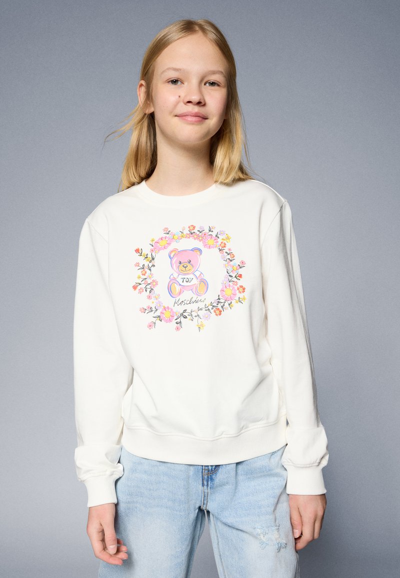Sudadera blanca con puños y dobladillo acanalados, que presenta un gráfico de un oso colorido rodeado de diseños florales. Estilo casual unisex.