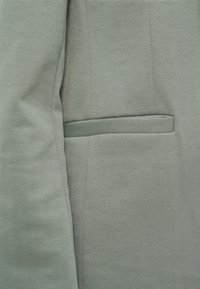 Close-up of grey herringbone fabric with a welt pocket detail on a tailored jacket sleeve and side.