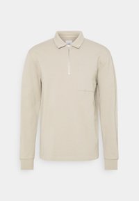 Polo à manches longues beige en coton. Présente un col zippé et une poche poitrine. Poignets côtelés avec une texture douce.
