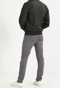 Szare spodnie o dopasowanym kroju, gładkiej fakturze i dwoma tylnymi kieszeniami, zestawione z ciemną kurtką. Całość uzupełniają białe trampki.