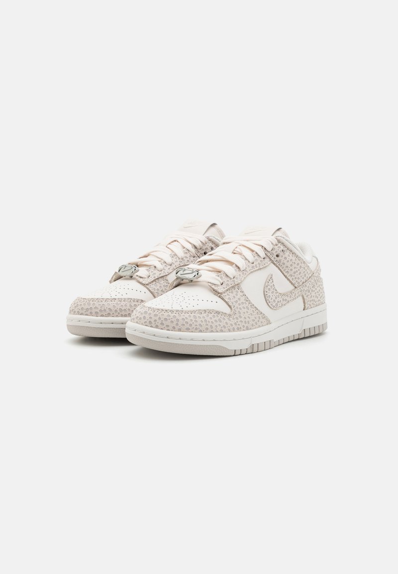 Zapatillas de deporte color beige claro con superposición texturizada, acentos de cuero suave, bloqueos de cordones circulares y suelas de goma blanca. Diseño de punta redondeada.