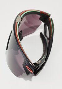 Sportliche Sonnenbrille mit schwarzem Rahmen, lila Gläsern sowie grünen und roten Akzenten. Verfügt über ein schlankes Design und gebogene Bügel für zusätzlichen Komfort.
