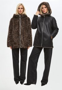 Két dzseki: az egyik barna, leopárdmintás műszőrme, a másik fekete műbőr. Mindkettő kapucnival rendelkezik, és fekete bő szárú farmerrel van párosítva.