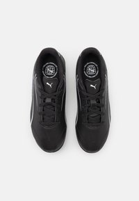 Scarpe sportive nere con una parte superiore liscia simile alla pelle, dettagli bianchi e una suola testurizzata. Presentano un design tradizionale con lacci e un dettaglio del logo.