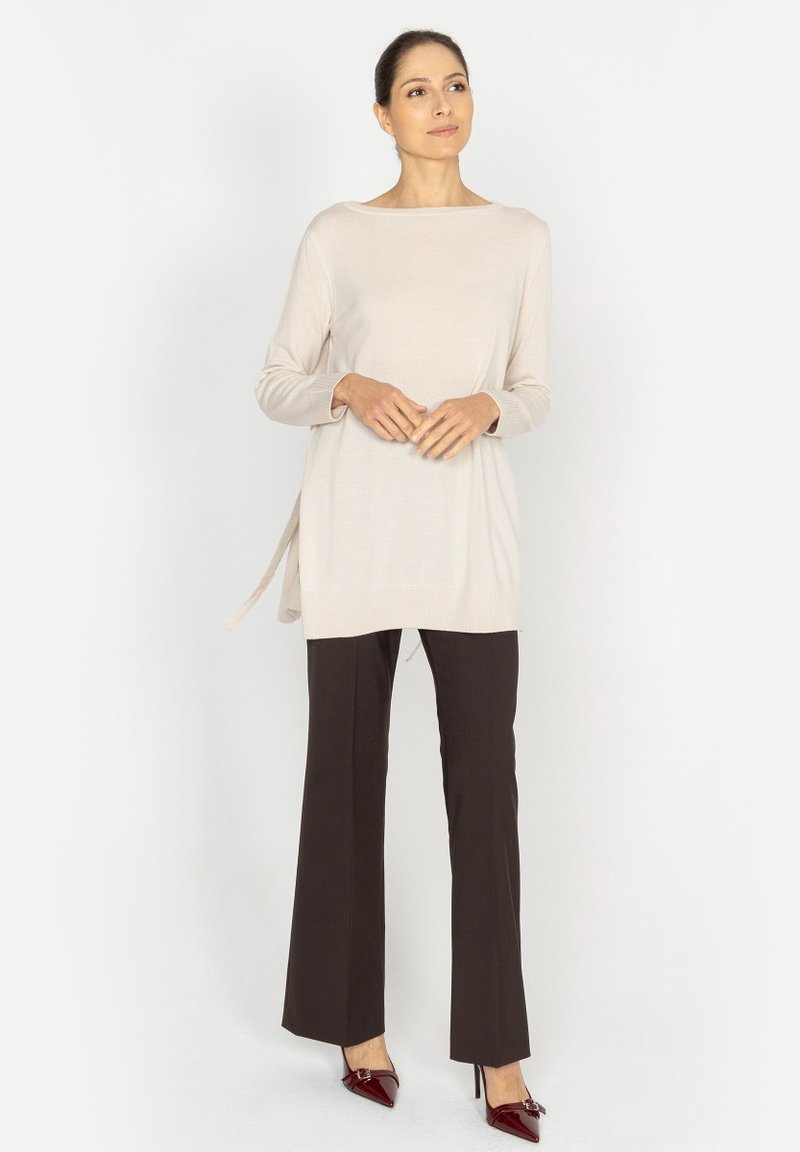 Jasno beżowa bluzka z długim rękawem i dekoltem w łódkę, połączona z ciemnobrązowymi spodniami i burgundowymi szpilkami. Posiada boczne wstążki jako detal dekoracyjny.