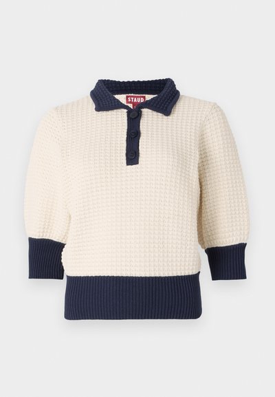 Pull en maille crème avec des accents bleu marine, doté d'un col polo, de trois boutons et de poignets et ourlet côtelés. Manches courtes texturées.