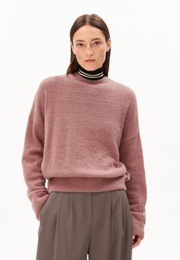 Rosa, gemütlicher Pullover mit rundem Ausschnitt und lockerer Passform, mit gerippten Bündchen und Saum. Getragen über einem schwarz-weißen gestreiften Rollkragenpullover.