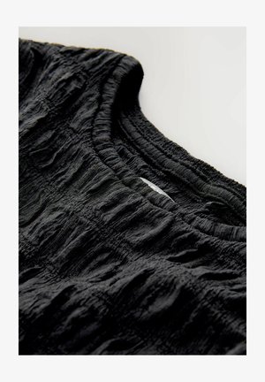 Juodas tekstūruotas audinys su raukšlėtu raštu. Yra susiraukšlėjęs apykaklė ir lygus vidus. Nėra matomų etikečių ar aparatūros.