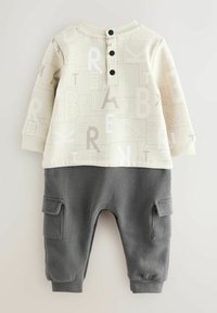 Dwuczęściowy strój składający się z kremowej bluzki z wzorami literowymi oraz szarych spodni z kieszeniami cargo, wykonany z miękkiej tkaniny z ściągaczami.