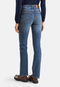 Jeans de denim en un lavado azul medio con corte recto, que cuentan con bolsillos traseros y un detalle de cinturilla de cuero marrón.
