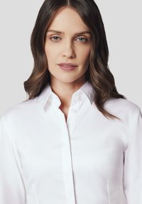 Biała koszula z guzikami, z klasycznym kołnierzykiem, wykonana z gładkiego materiału, z długimi rękawami, delikatnie dopasowana, z czystym wykończeniem i bez widocznych wzorów.