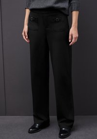 Pantaloni neri a gamba larga realizzati in tessuto morbido, con due tasche posteriori decorate con fibbie e una vestibilità sartoriale.