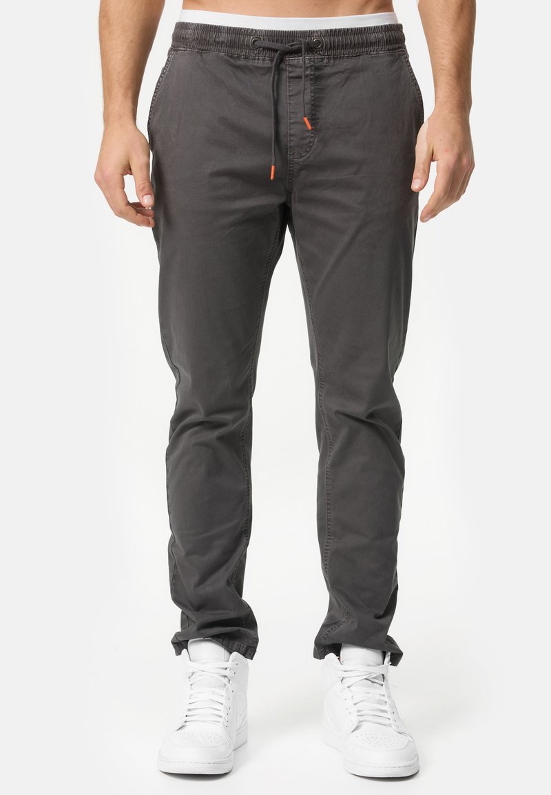 Pantalones grises de tiro alto con cintura elástica y cordón, de corte ajustado y con bolsillos laterales, combinados con zapatillas altas blancas.