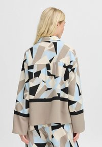 Multi gekleurde abstracte jas met patronen van geometrische vormen in blauw, beige en zwart, met een relaxed fit en zachte textuur.