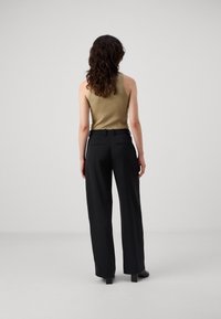 Ein tanfarbener, gerippter Tanktop, kombiniert mit weit geschnittenen, hochtaillierten schwarzen Hosen. Die Hosen besitzen eine glatte Textur und Gesäßtaschen.