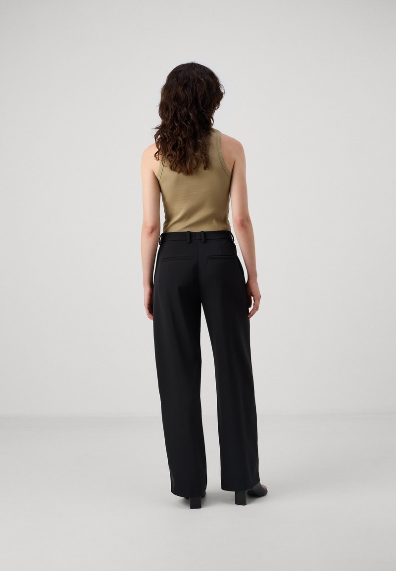Tan geribd tanktop gecombineerd met hoge taille, brede zwarte broek. De broek heeft een gladde textuur en achterzakken.