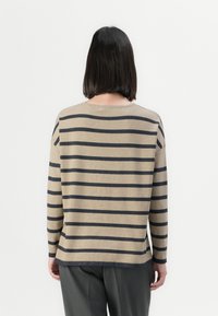 Beige genser med marineblå striper, lange ermer, rund hals og avslappet passform. Har en litt lengre bakhem. Laget av mykt strikket materiale.