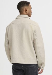 Beige uldblandet jakke med krave, rygåge og lange ærmer. Har knaplukning ved ærmerne og en afslappet pasform. Struktureret finish, ingen mønstre.
