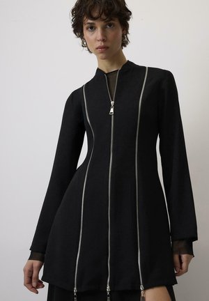 Mustast kleidist kõrge kaelusega, pikkade varrukatega ning neli hõbedast zigipidi, mis kulgevad piki esiosa. Tehtud siledast kangast, millel on keha lähedane siluett.