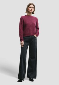 Suéter de punto burdeos con un corte relajado, combinado con jeans negros de pierna ancha que presentan sutiles adornos. Completado con tacones negros.