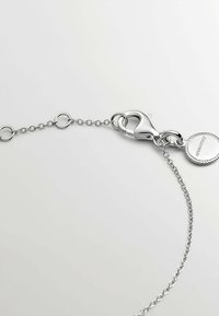 Cadena de metal plateado con un cierre y una etiqueta circular. La cadena presenta eslabones ovalados y una textura suave, con un acabado brillante y pulido.