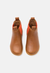 Botas de tobillo de cuero marrón con un panel elástico naranja a los lados. Textura suave, punta redonda y tiradores para facilitar el uso.