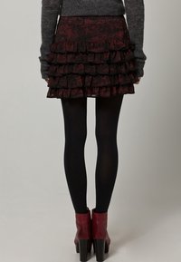 Svart och vinröd volangminikjol med flera lager, bärs med svarta strumpbyxor och vinröda ankelskot med tjock klack.