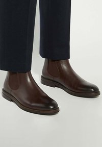 Brown leather Chelsea boots with elastic side panels and rounded toe. Smooth texture, low block heel, and decorative seam along the sole.