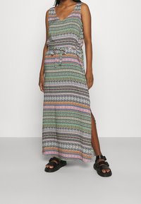 Maxi-jurk met een V-hals, meerkleurige geometrische patronen, mouwloos ontwerp, getailleerde taille en een zijsplit. Gecombineerd met zwarte sandalen.