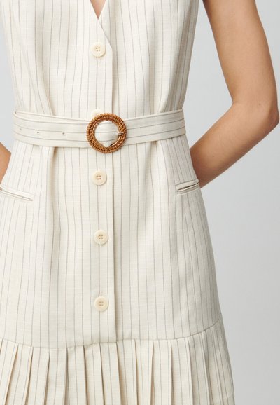 Robe à rayures ivoire avec un col en V, des boutons à l'avant, des poches latérales et une ceinture tressée avec une boucle ronde. Texture plissée à l'ourlet.