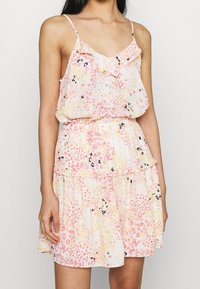 Kwiatowa mini sukienka w różowe, żółte i czarne wzory. Wykonana z lekkiego materiału, z cienkimi ramiączkami i falbaniastego dekoltu.