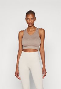 Sujetador deportivo en un suave beige con una textura lisa y estriada y tirantes anchos. Combinado con leggings de tiro alto en beige claro, también estriados.