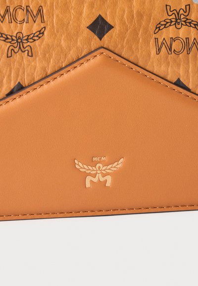 Article en cuir fauve avec rabat triangulaire cousu, présentant le logo MCM embossé avec une couronne de laurier et des motifs de diamants noirs et d'emblèmes sur un fond texturé.