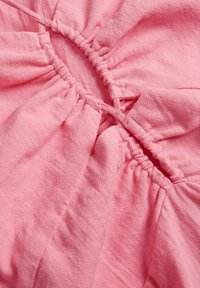 Tela rosa con textura fruncida, con un cierre de cordón. Material suave y ligero con un brillo sutil y costuras visibles.