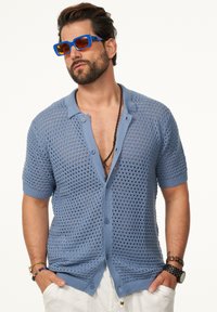 Himmelblaues, gestricktes Polohemd mit kurzen Ärmeln, das ein strukturiertes offenes Gewebe, eine Knopfleiste und gerippte Bündchen aufweist.