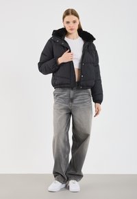 Zwarte pufferjack met een bontgevoerde capuchon, gecapitonneerd ontwerp en elastische manchetten, gecombineerd met high-waisted, vervaagde grijze jeans en witte sneakers.