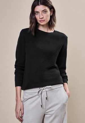 Maglione nero a coste con texture diagonale a contrasto, scollo rotondo e maniche lunghe, abbinato a pantaloni della tuta grigi chiari.