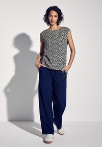 Pantaloni blu navy dalla vestibilità ampia abbinati a una maglietta a maniche corte con motivo floreale in crema e nero. Sneakers bianche.