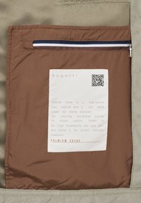 Brown fabric with a zip pocket on the left and label detailing "Premium Suede" stitched on an inner lining of soft beige material.