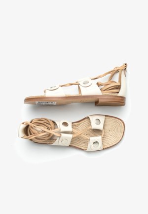Sandales plates blanches avec semelles en corde tressée, brides en cuir avec boutons argentés et lacets beiges à nouer autour de la cheville, posées côte à côte.