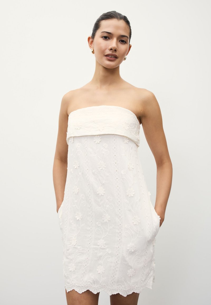 Robe blanche bustier avec broderie florale, ourlet festonné et poches latérales. Confectionnée dans un tissu léger à la texture douce.