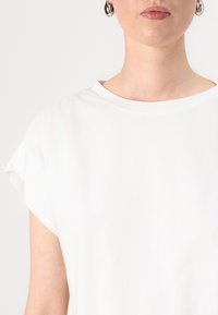 Bílé bavlněné tričko s kulatým výstřihem a kratkými rukávy s ohrnutím. Hladká textura, minimalistický styl a žádné viditelné vzory nebo akcenty.